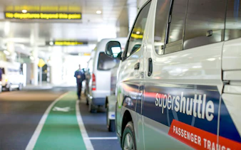Super Shuttle vans lined up at airport terminal for passenger transfers.