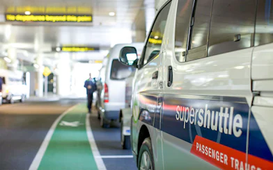 Super Shuttle vans lined up at airport terminal for passenger transfers.