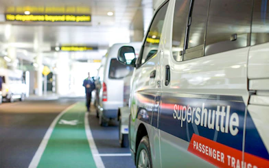 Super Shuttle vans lined up at airport terminal for passenger transfers.