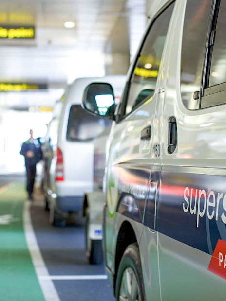 Super Shuttle vans lined up at airport terminal for passenger transfers.