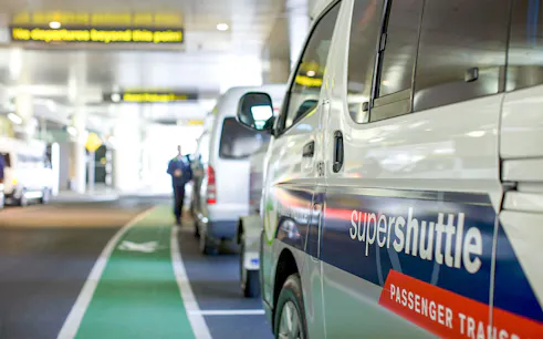 Super Shuttle vans lined up at airport terminal for passenger transfers.