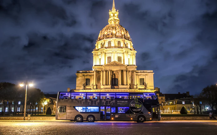 Les Invalides illuminated at night with a tour bus in Paris.