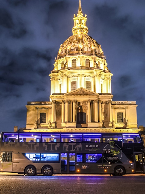 Les Invalides illuminated at night with a tour bus in Paris.