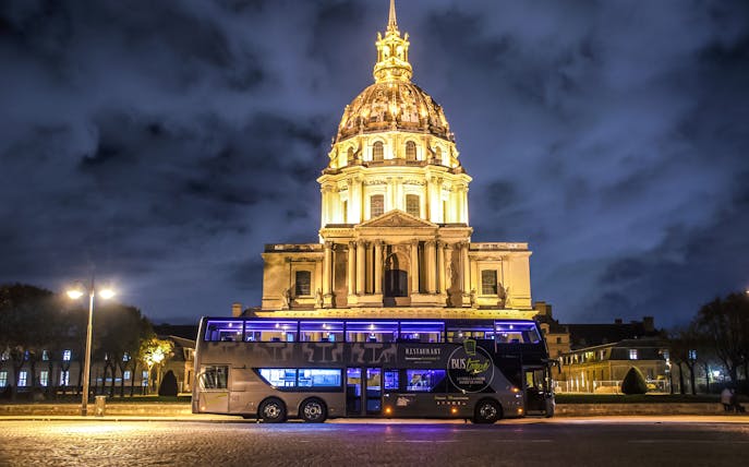 Les Invalides illuminated at night with a tour bus in Paris.