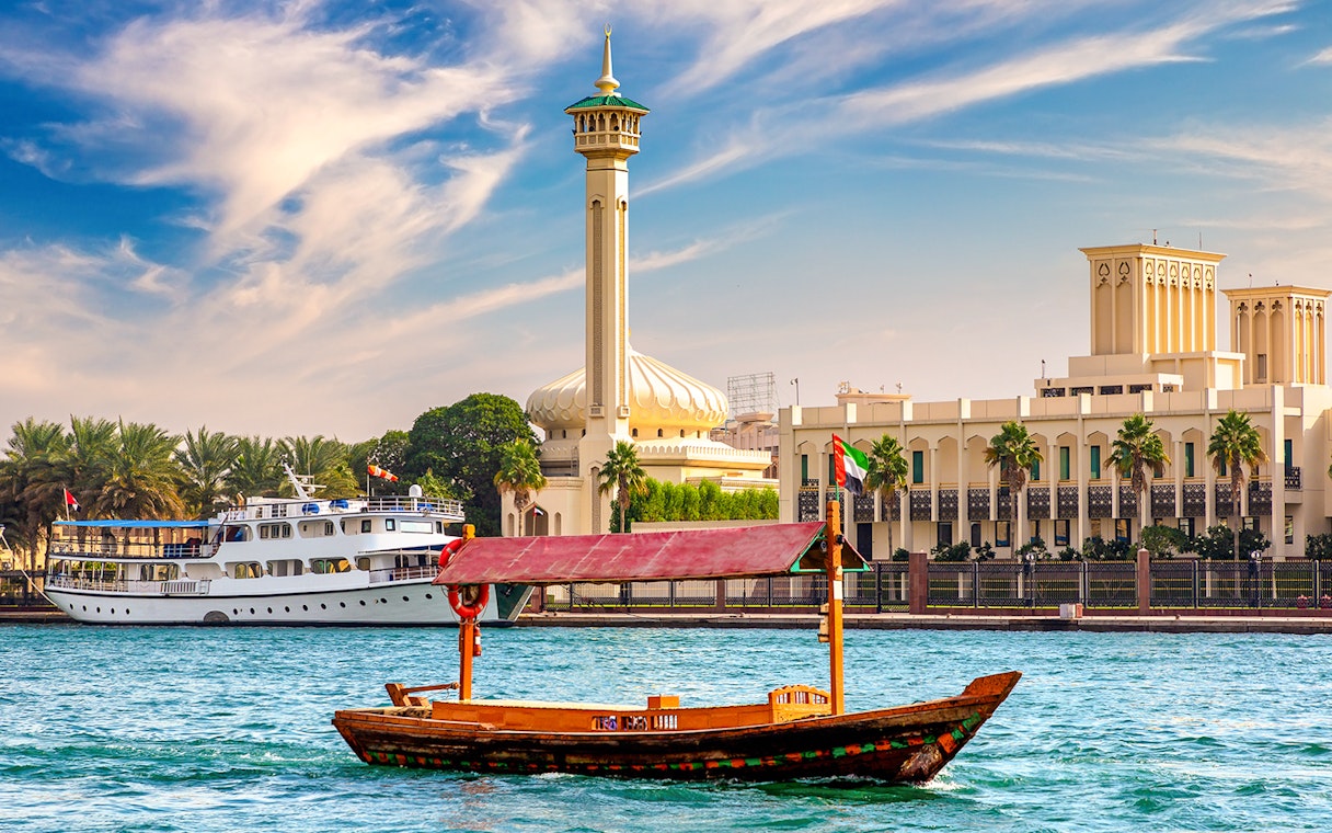 Wooden Abra boat on Dubai Canal with mosque and buildings in the background.