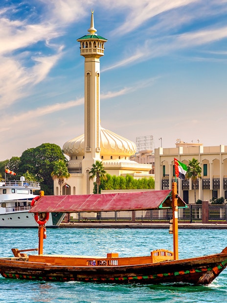 Wooden Abra boat on Dubai Canal with mosque and buildings in the background.