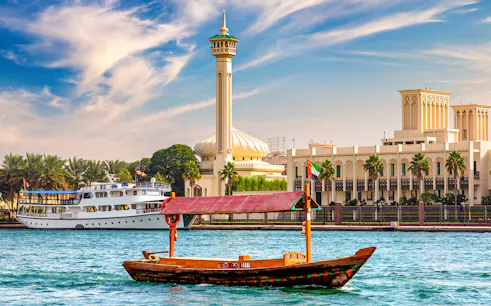 Wooden Abra boat on Dubai Canal with mosque and buildings in the background.