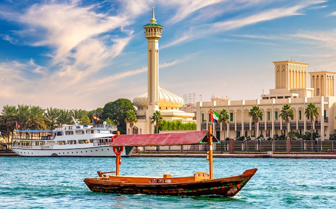 Wooden Abra boat on Dubai Canal with mosque and buildings in the background.