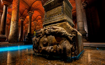 Medusa Head sculpture in Basilica Cistern, Istanbul, surrounded by illuminated columns.