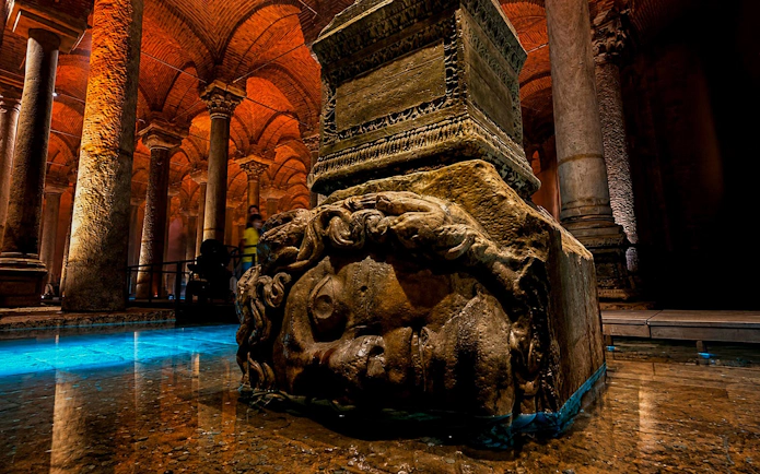 Medusa Head sculpture in Basilica Cistern, Istanbul, surrounded by illuminated columns.