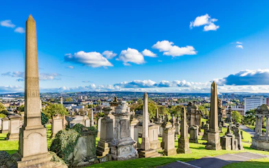 Victorian tombstones and obelisks at Glasgow Necropolis, overlooking the cityscape of Glasgow, Scotland.