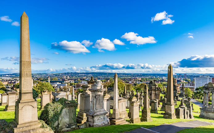 Victorian tombstones and obelisks at Glasgow Necropolis, overlooking the cityscape of Glasgow, Scotland.