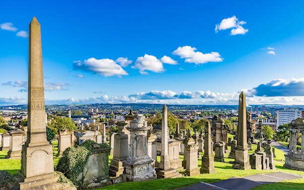 Victorian tombstones and obelisks at Glasgow Necropolis, overlooking the cityscape of Glasgow, Scotland.