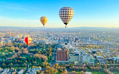 Hot air balloons floating over Melbourne cityscape at sunrise.