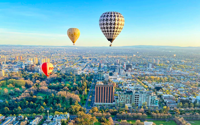 Hot air balloons floating over Melbourne cityscape at sunrise.