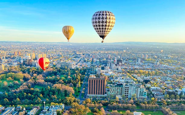 Hot air balloons floating over Melbourne cityscape at sunrise.