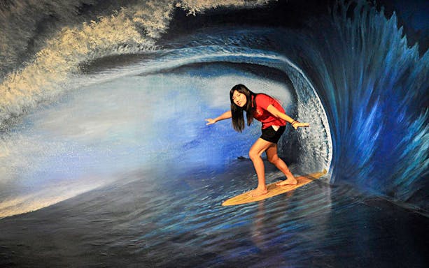Person posing on a surfboard in a 3D wave mural at Alive 3D Art Gallery, Port Dickson.
