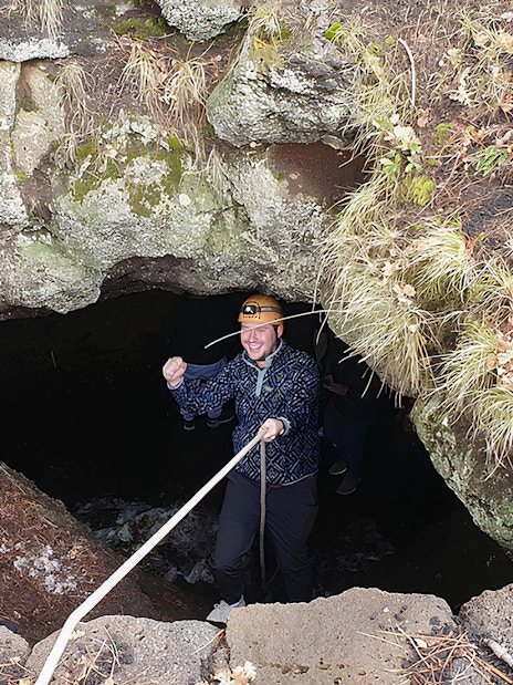 Tourists with helmets entering a lava cave guided by an instructor holding a rope.