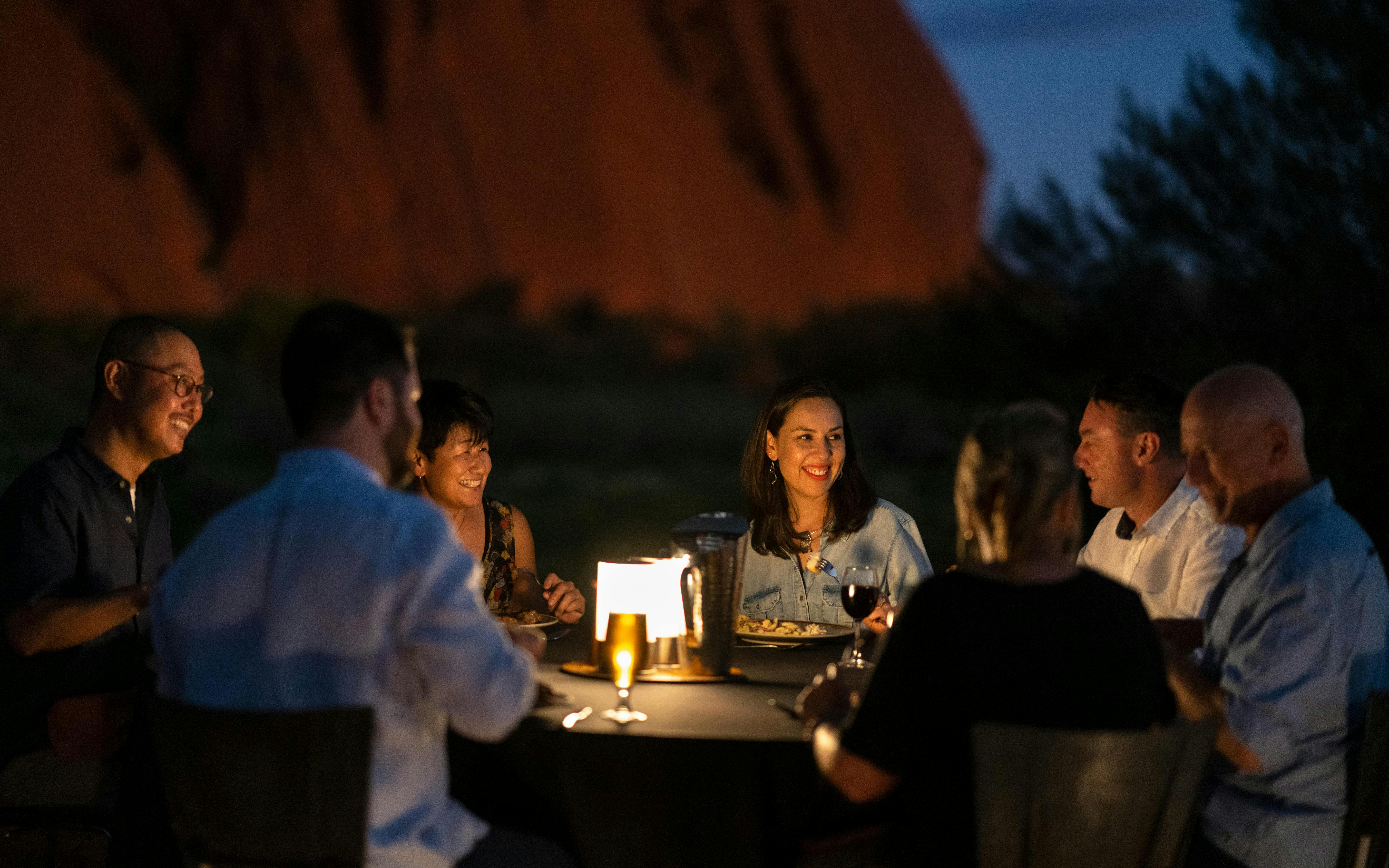 Group dining outdoors at Uluru during sunset on a stargazing tour with BBQ dinner.