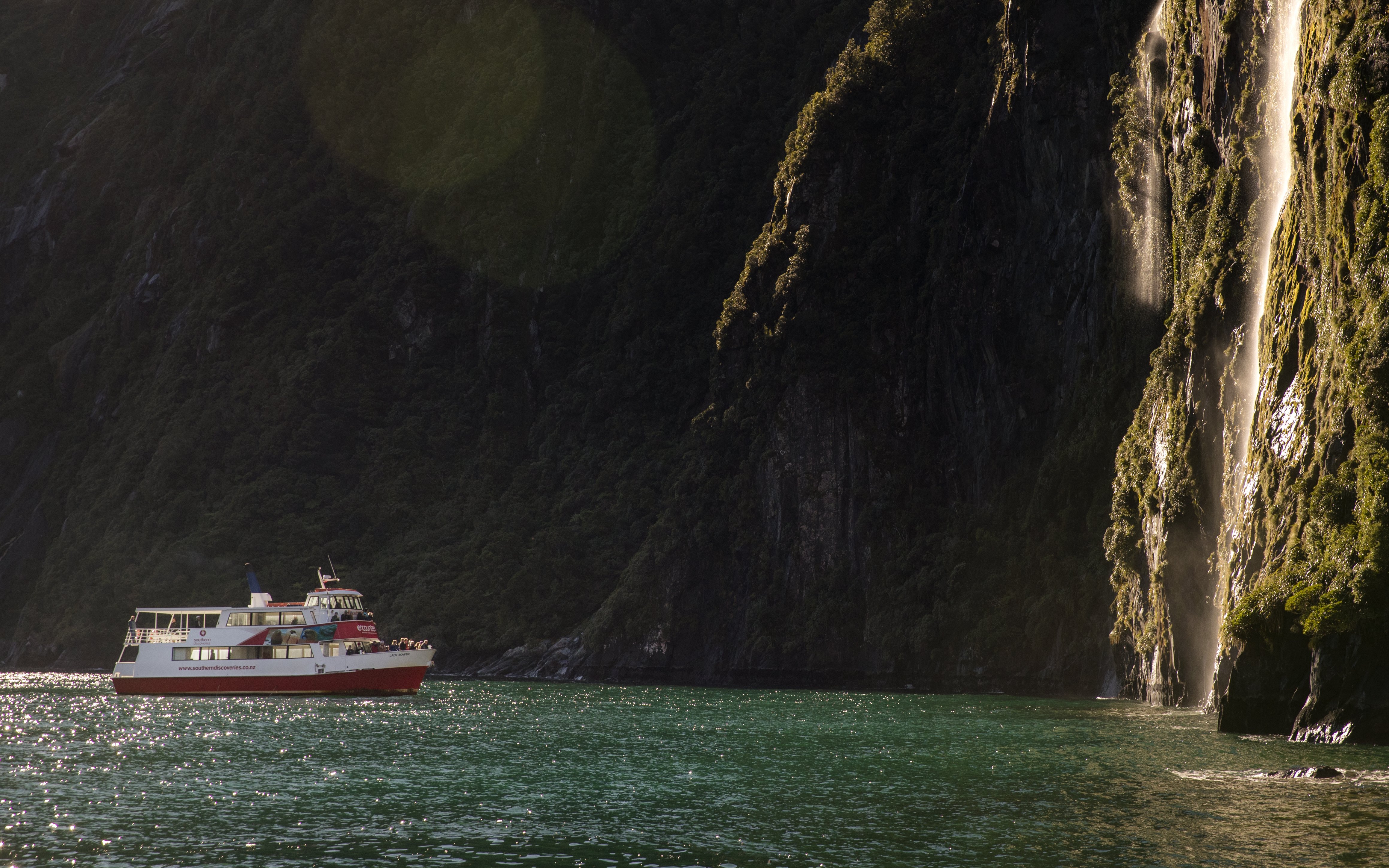Cruise boat near waterfall in Milford Sound, New Zealand.
