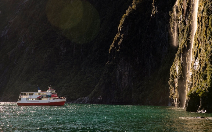 Cruise boat near waterfall in Milford Sound, New Zealand.