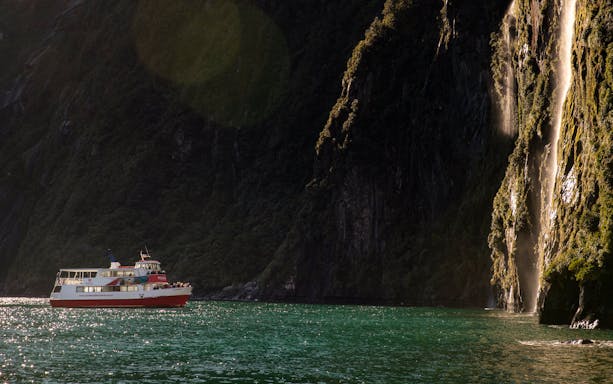Cruise boat near waterfall in Milford Sound, New Zealand.