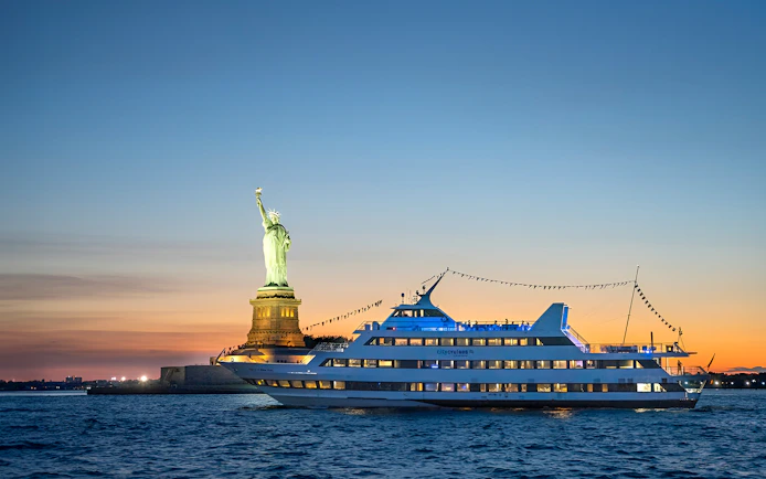 Dinner cruise boat sailing past the Statue of Liberty at sunset.
