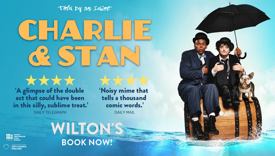 Charlie & Stan performers sitting on a barrel with a dog, holding an umbrella.