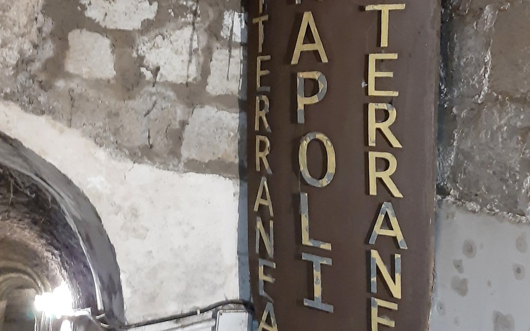 Entrance sign to Naples Underground with stone wall background.