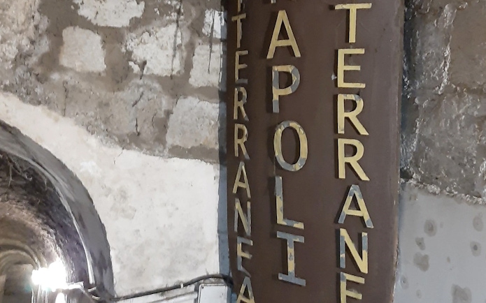 Entrance sign to Naples Underground with stone wall background.