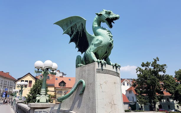 Dragon statue on Dragon Bridge in Ljubljana, Slovenia, with cityscape in the background.