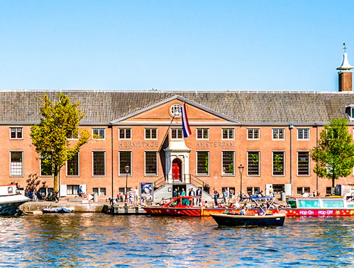 H'ART Museum exterior with canal view in Amsterdam, featuring boats and historic architecture.