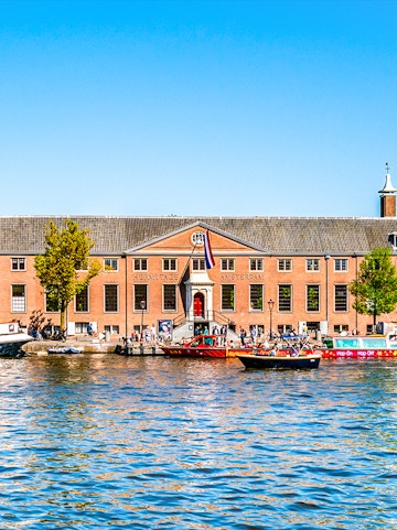 H'ART Museum exterior with canal view in Amsterdam, featuring boats and historic architecture.
