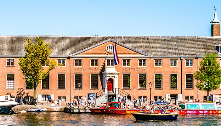 H'ART Museum exterior with canal view in Amsterdam, featuring boats and historic architecture.