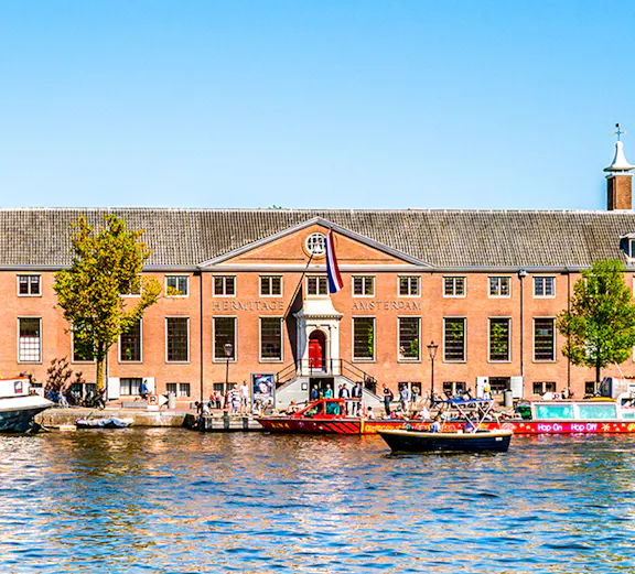 H'ART Museum exterior with canal view in Amsterdam, featuring boats and historic architecture.