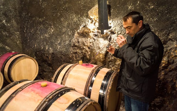 Man sampling wine from barrels in Tvrdoš monastery cellar, Bosnia and Herzegovina.
