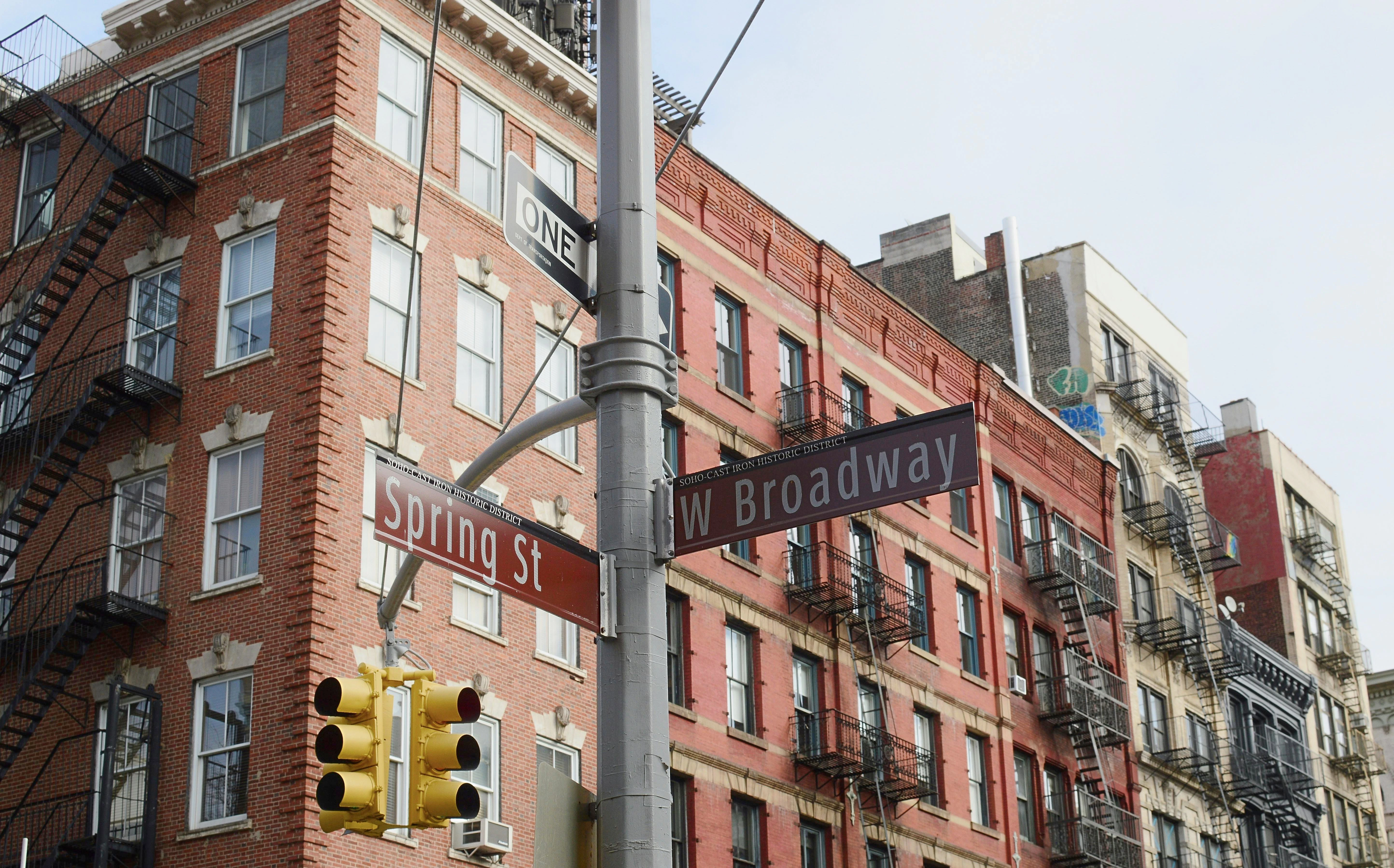 Spring Street and West Broadway signs with historic SoHo apartment buildings in New York City.