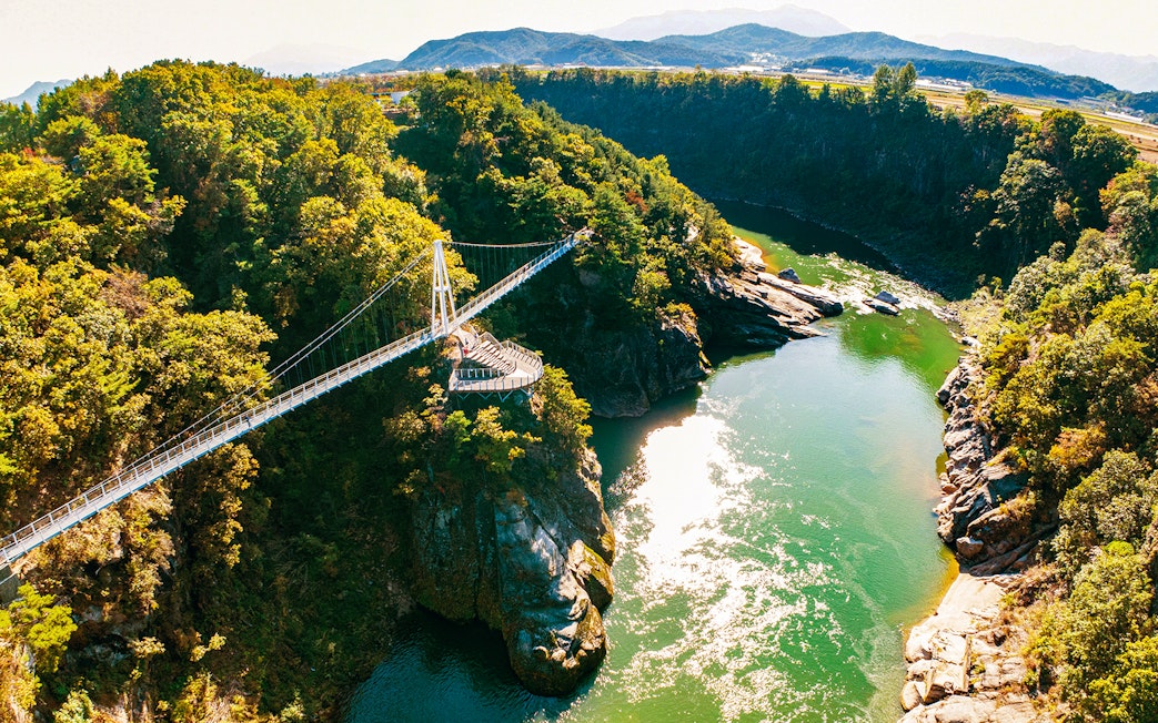 Suspension bridge over lush valley and river on DMZ 2nd Tunnel & Cliffside Path tour.