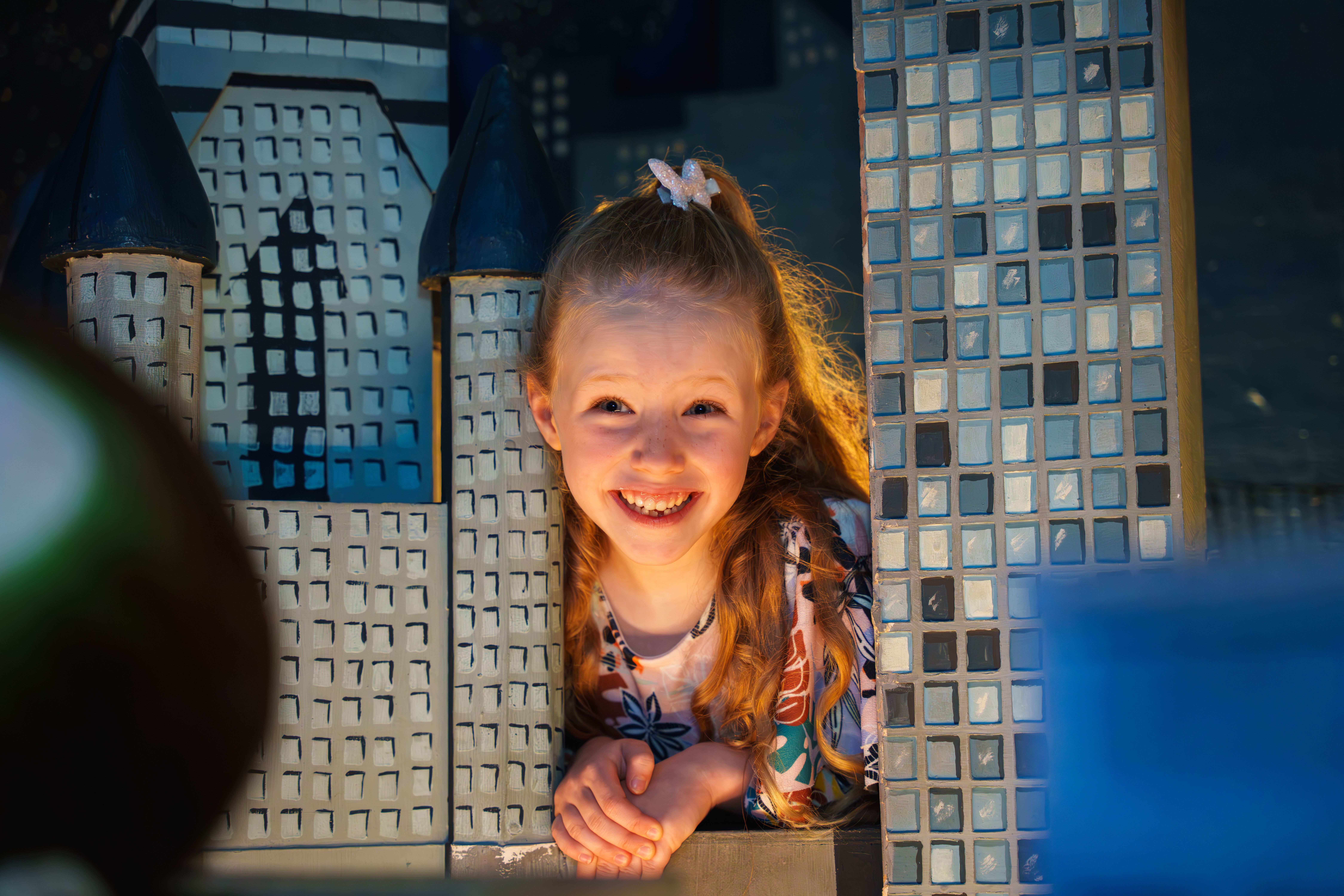 Child smiling through a model cityscape at the National Wax Museum.