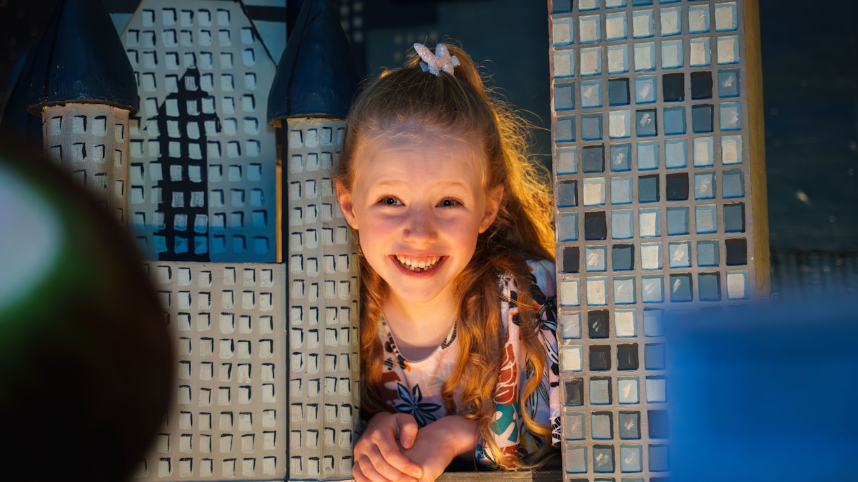 Child smiling through a model cityscape at the National Wax Museum.