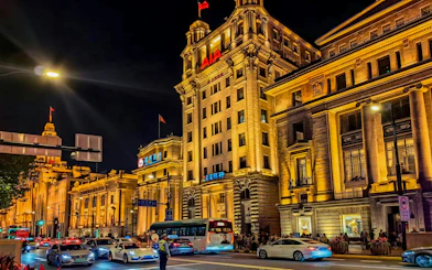 Night view of illuminated historic buildings along the Bund in Shanghai, China, with traffic on the street.