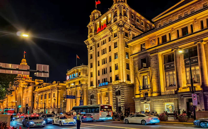 Night view of illuminated historic buildings along the Bund in Shanghai, China, with traffic on the street.
