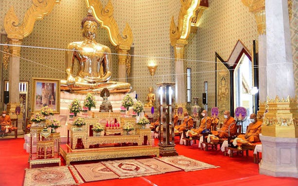 Golden Buddha statue inside Marble Temple, Bangkok, with monks seated in prayer.