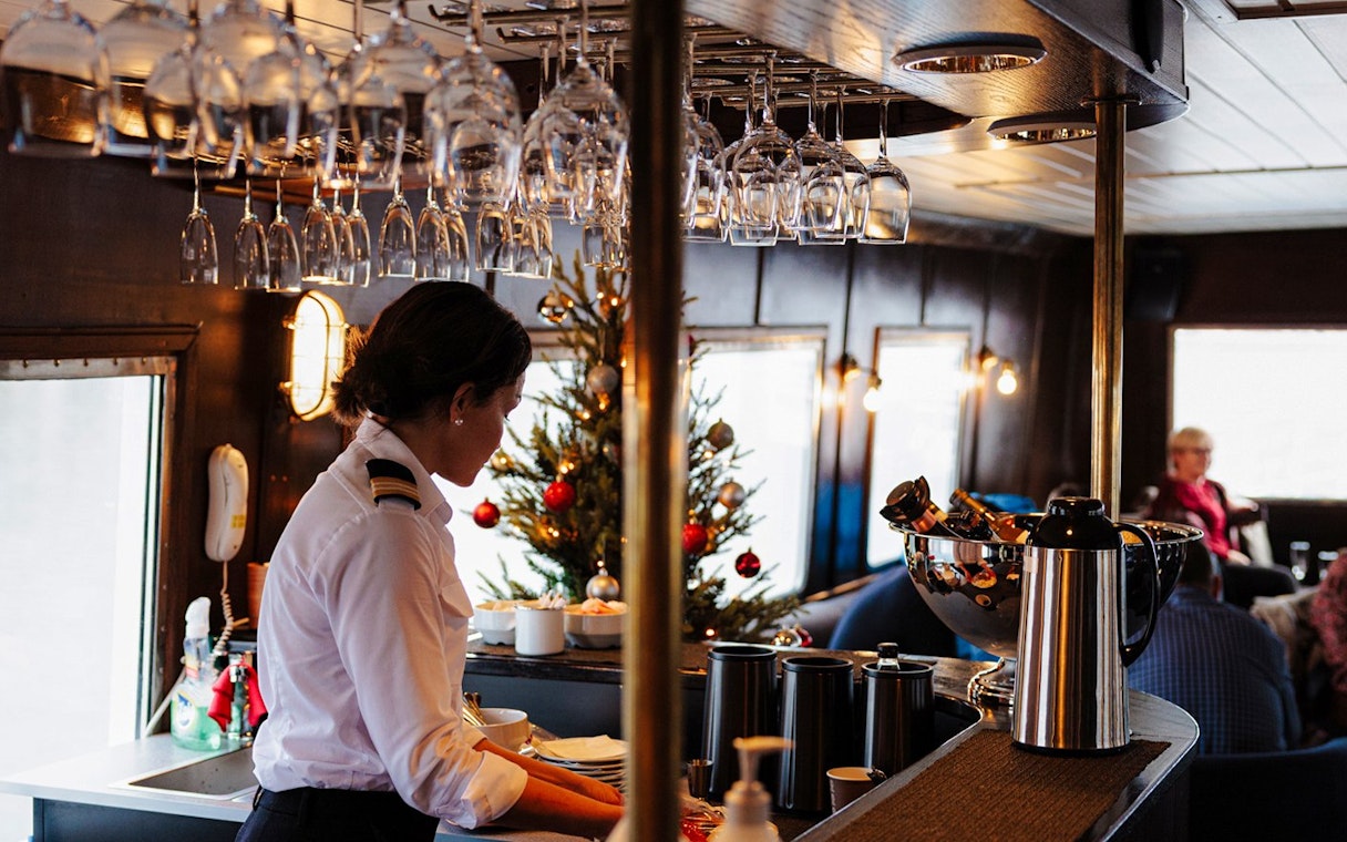 Bar area on a sightseeing cruise in Hjørundfjord, Norway, with a crew member preparing drinks.