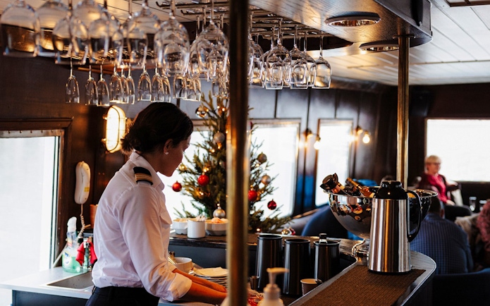 Bar area on a sightseeing cruise in Hjørundfjord, Norway, with a crew member preparing drinks.