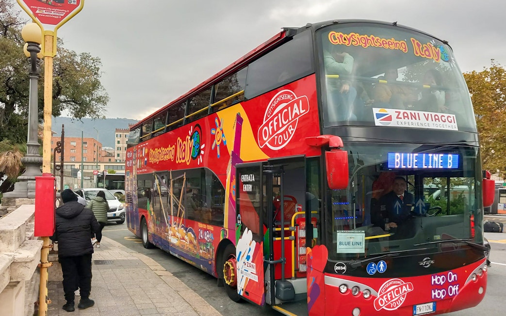 Hop-on hop-off tour bus in Genoa, Italy, with passengers boarding.