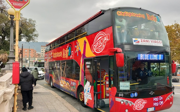 Hop-on hop-off tour bus in Genoa, Italy, with passengers boarding.