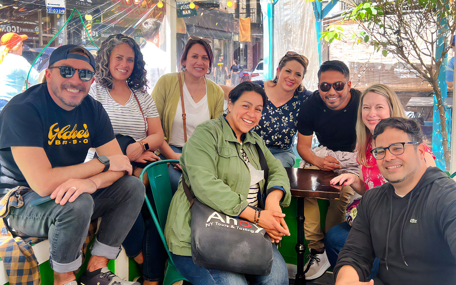 Tourists with guide on Ahoy New York Food Tour, smiling at an outdoor cafe.