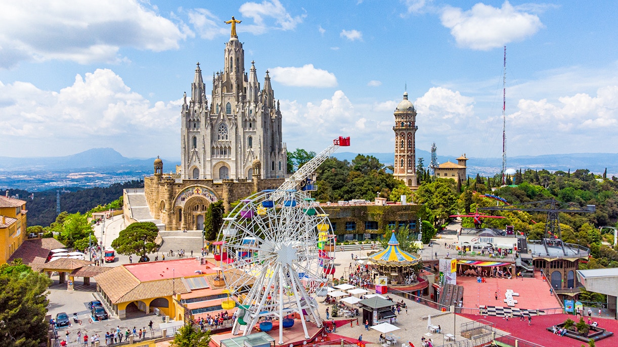 Tibidabo amusement park rides with panoramic view of Barcelona cityscape.