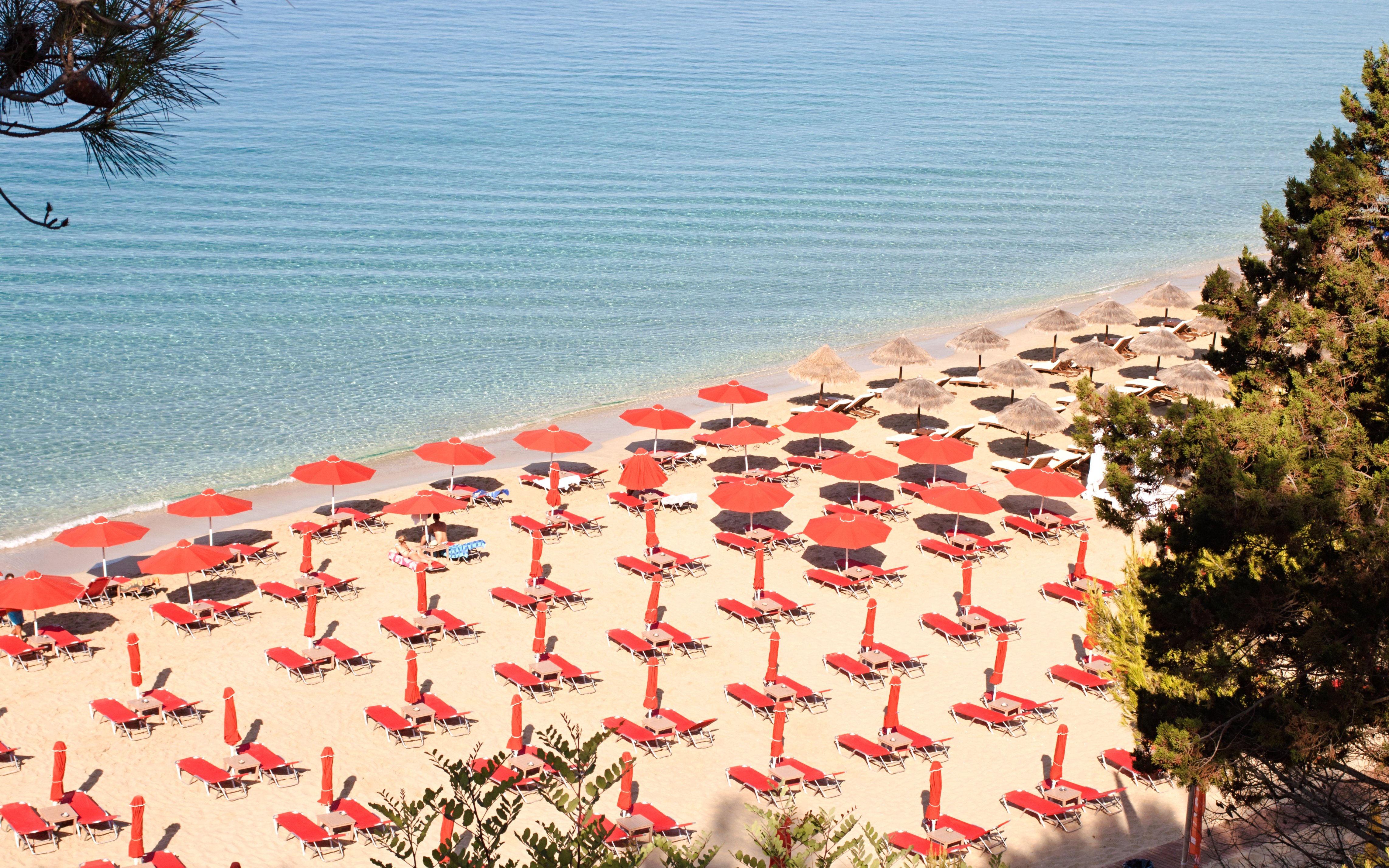 Sun loungers and red umbrellas on Makris Gialos beach, Argostoli, Kefalonia, Greece.